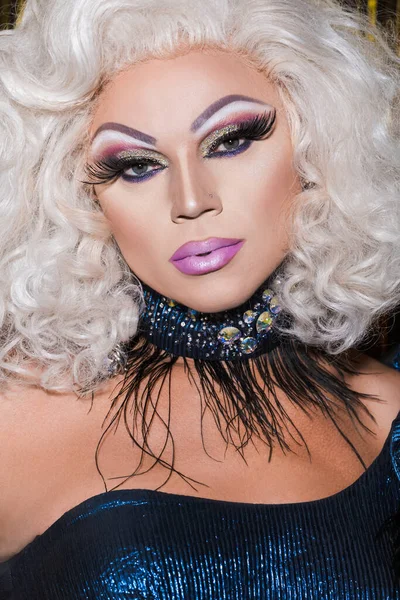 Retrato de drag queen con maquillaje brillante, en peluca rubia y collar de purpurina - foto de stock
