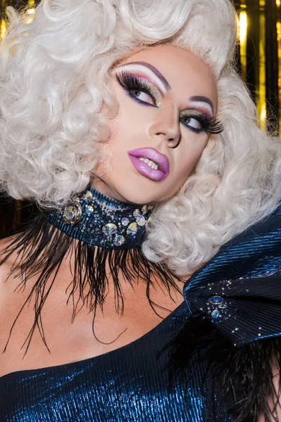 Eccentric transgender person with bright makeup posing in wig and shiny necklace on shiny background — Stock Photo