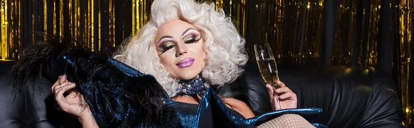 Zufriedene Drag Queen in blonder Perücke mit Champagnerglas auf glänzendem Hintergrund, Banner — Stockfoto