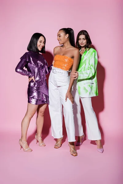 Full length of interracial women in trendy outfits smiling near friend on pink — Stock Photo