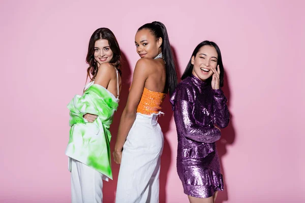 Alegres mujeres multiétnicas en trajes de moda posando en rosa — Stock Photo