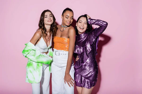 Mujeres multiétnicas positivas en trajes de moda posando en rosa - foto de stock