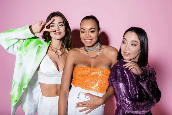 Sonrientes mujeres interracial en trajes de moda posando en rosa - foto de stock