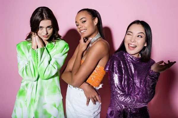 Mujeres interracial positivas en trajes de moda posando en rosa - foto de stock