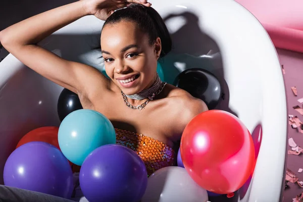 High angle view of pleased african american woman lying in bathtub with colorful balloons — Stock Photo