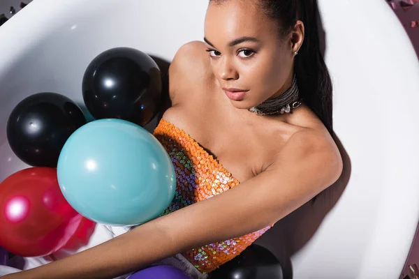 High angle view of brunette african american model lying in bathtub with balloons — Stock Photo