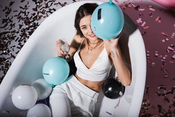 Vue de dessus de la femme souriante avec tatouage couché dans la baignoire tout en tenant ballon et verre de champagne — Photo de stock