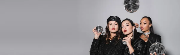 Young woman in beret posing near interracial models holding disco balls on grey, banner — Stock Photo