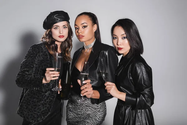 Young multiethnic models holding glasses of champagne on grey — Stock Photo