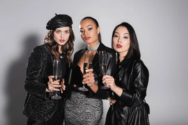 Young multiethnic women holding glasses of champagne on grey — Stock Photo