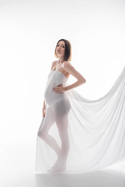 Jeune femme enceinte en tissu posant sur fond gris — Photo de stock