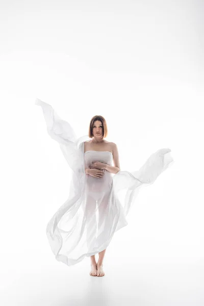 Полная длина беременной женщины в ткани касаясь живота на сером фоне — стоковое фото
