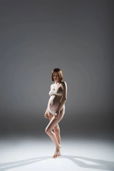 Повна довжина брюнетки вагітна жінка вгорі і трусики на сірому фоні — стокове фото