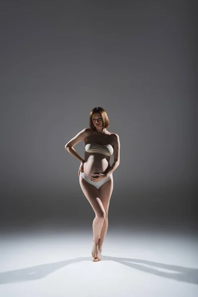 Повна довжина вагітної жінки в трусиках і зверху стоячи на сірому фоні — стокове фото