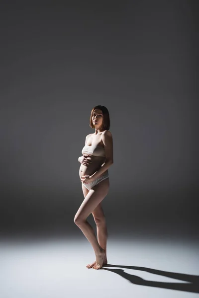 Donna incinta a piedi nudi in biancheria intima in piedi su sfondo grigio con ombra — Foto stock