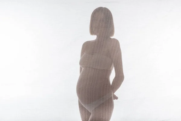 Schwangere in Unterwäsche posiert in Stoffnähe auf grauem Hintergrund — Stockfoto