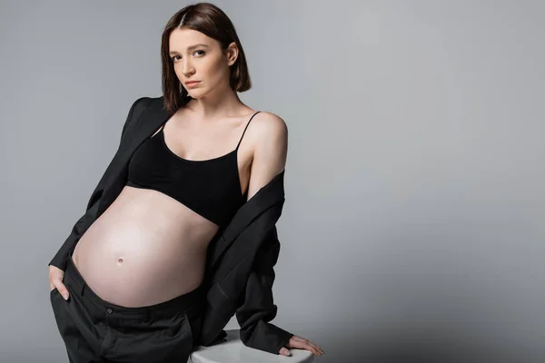 Pregnant woman in top and suit standing near chair isolated on grey — Stock Photo
