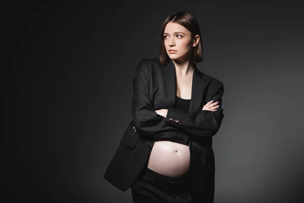 Elegante modelo embarazada cruzando brazos aislados en gris oscuro - foto de stock