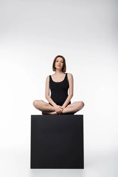 Pregnant woman in swimsuit sitting on black cube on white background — Stock Photo