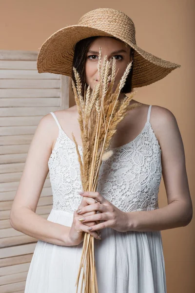 Pregnant woman in sun hat holding spikelets near face isolated on beige — Stock Photo
