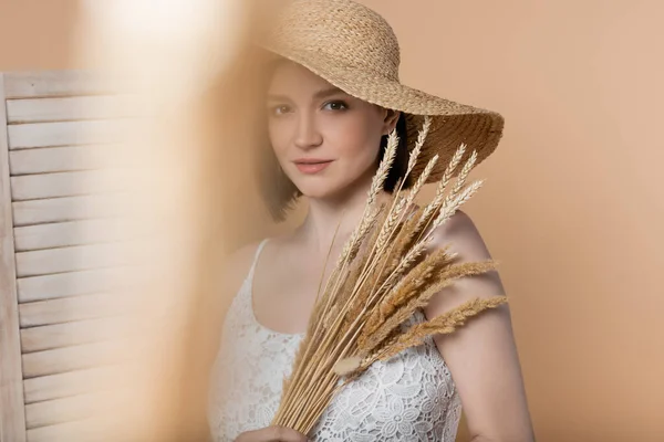 Frau mit Strohhut und Kleid hält Stacheln in der Nähe von Klappschirm isoliert auf beige — Stockfoto