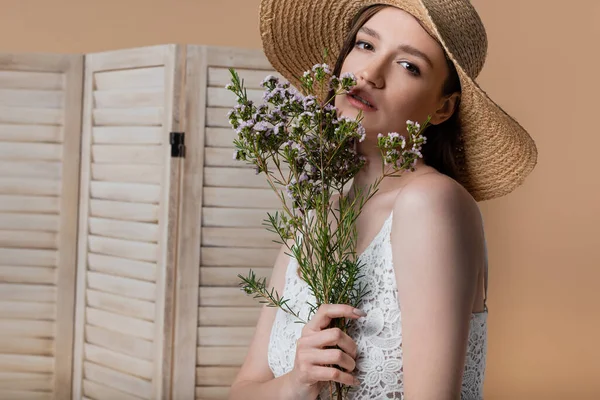 Junge Frau im Kleid mit Blumen in der Nähe von verschwommenem Klappbildschirm isoliert auf beige — Stockfoto