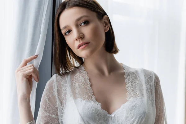 Young woman in bra looking at camera near curtains at home — Stock Photo
