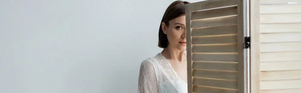 Young brunette woman looking at camera near folding screen, banner — Stock Photo