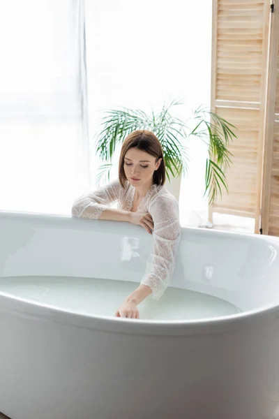 Jolie femme touchant l'eau dans la baignoire dans la salle de bain — Photo de stock