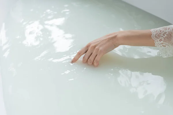 Vue recadrée de la femme touchant l'eau dans la baignoire dans la salle de bain — Photo de stock