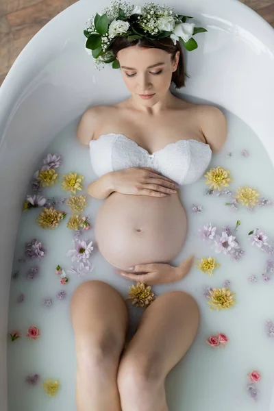 Vista superior de la mujer embarazada tomando baño con flores y leche en casa - foto de stock