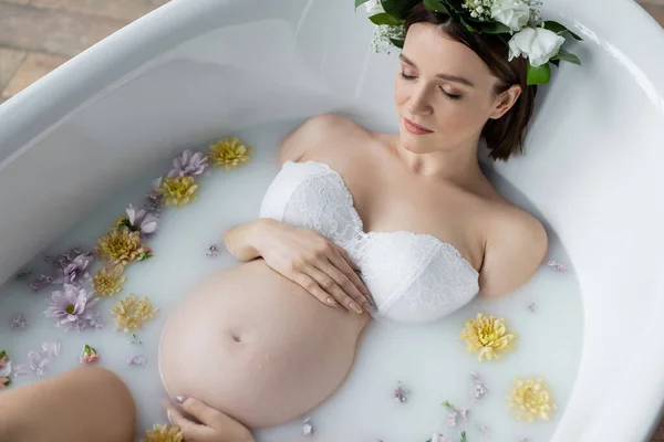 Visão superior da mulher grávida no sutiã tomando banho com flores e leite em casa — Fotografia de Stock