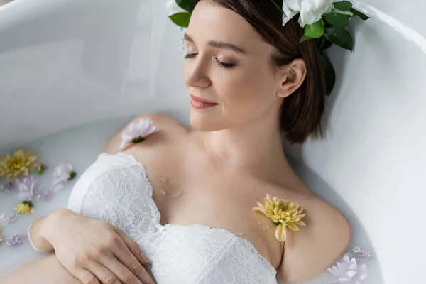 Jovem mulher no sutiã tomando banho com flores e leite em casa — Fotografia de Stock