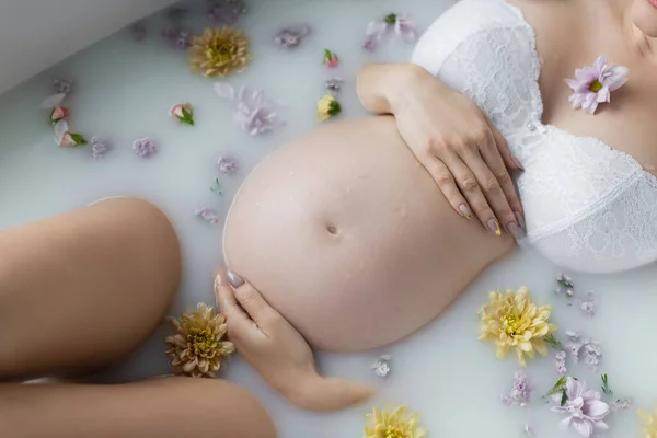 Cropped view of pregnant woman taking bath with flowers and milk — Stock Photo
