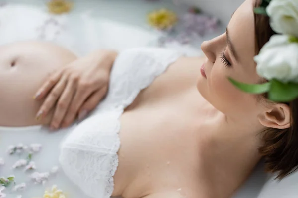Visão de alto ângulo da mulher grávida tocando barriga embaçada no banho com flores e leite em casa — Fotografia de Stock