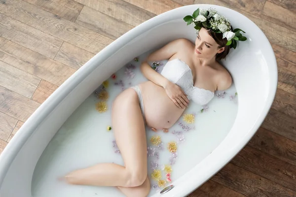 Вид сверху беременной женщины в венке, расслабляющейся в молочной ванне дома — стоковое фото