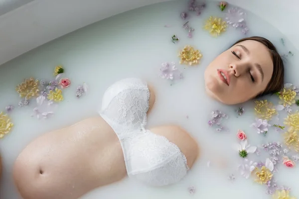 Vista superior de la mujer embarazada con los ojos cerrados relajante en baño de leche con flores - foto de stock