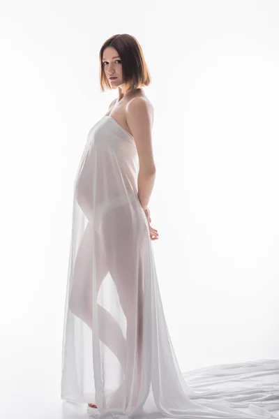 Full length of barefoot pregnant woman posing in fabric on white background — Stock Photo