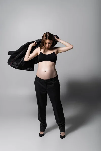Модная беременная женщина в пиджаке на сером фоне — стоковое фото