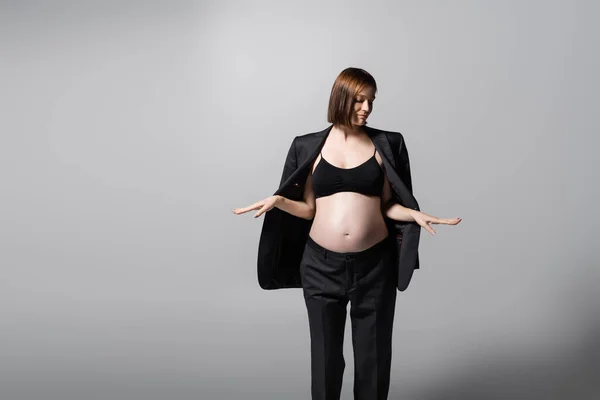 Brünette schwangere Frau im Anzug und Top posiert auf grauem Hintergrund — Stockfoto