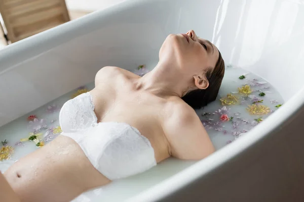 Mulher grávida em sutiã de renda relaxante no banho de leite com flores — Fotografia de Stock