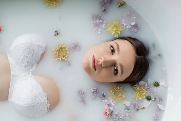 Вид сверху симпатичной женщины, смотрящей в камеру, принимая молочную ванну с цветами — стоковое фото