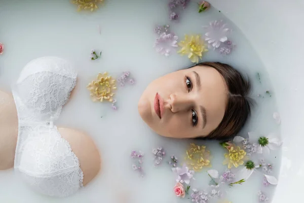 Vista dall'alto della bella donna che guarda la fotocamera mentre prende il bagno di latte con i fiori — Foto stock