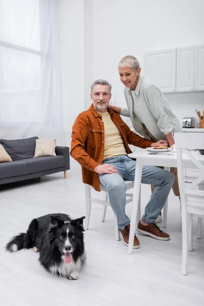 Fröhliches Paar schaut beim Frühstück in der Küche auf Border Collie — Stockfoto