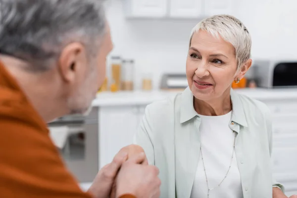 Blurred mature man holding hand of smiling wife in kitchen — Stock Photo