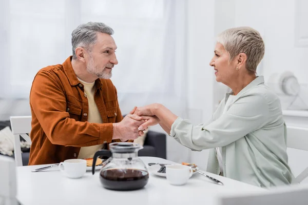 Couple positif tenant la main près du café et des crêpes dans la cuisine — Photo de stock