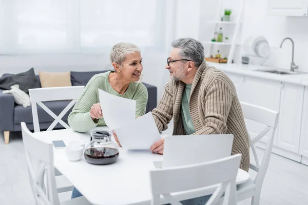 Glückliche Seniorin hält Dokument neben Ehemann und Geräten in Küche — Stockfoto