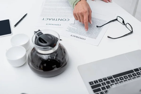 Vista recortada de la mujer mayor señalando el contrato cerca de gadgets y café en la cocina - foto de stock