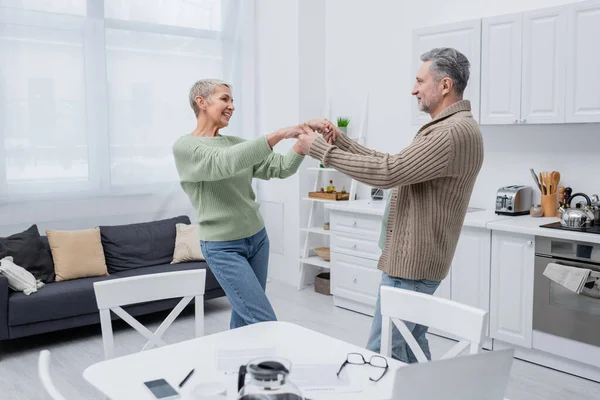 Positive couple dancing near papers and devices in kitchen — Stock Photo