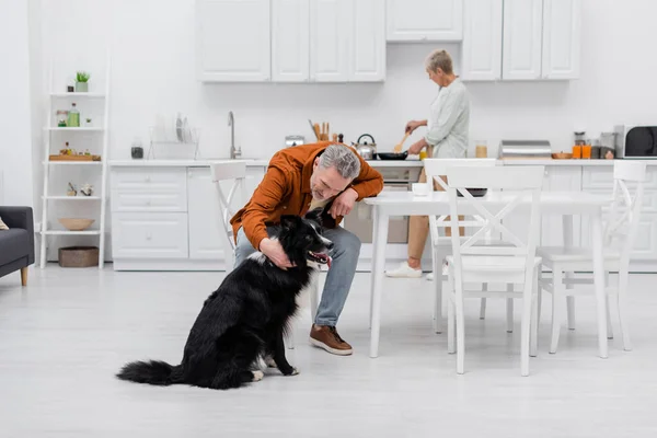 Uomo di mezza età petting border collie vicino tazza di caffè in cucina — Foto stock